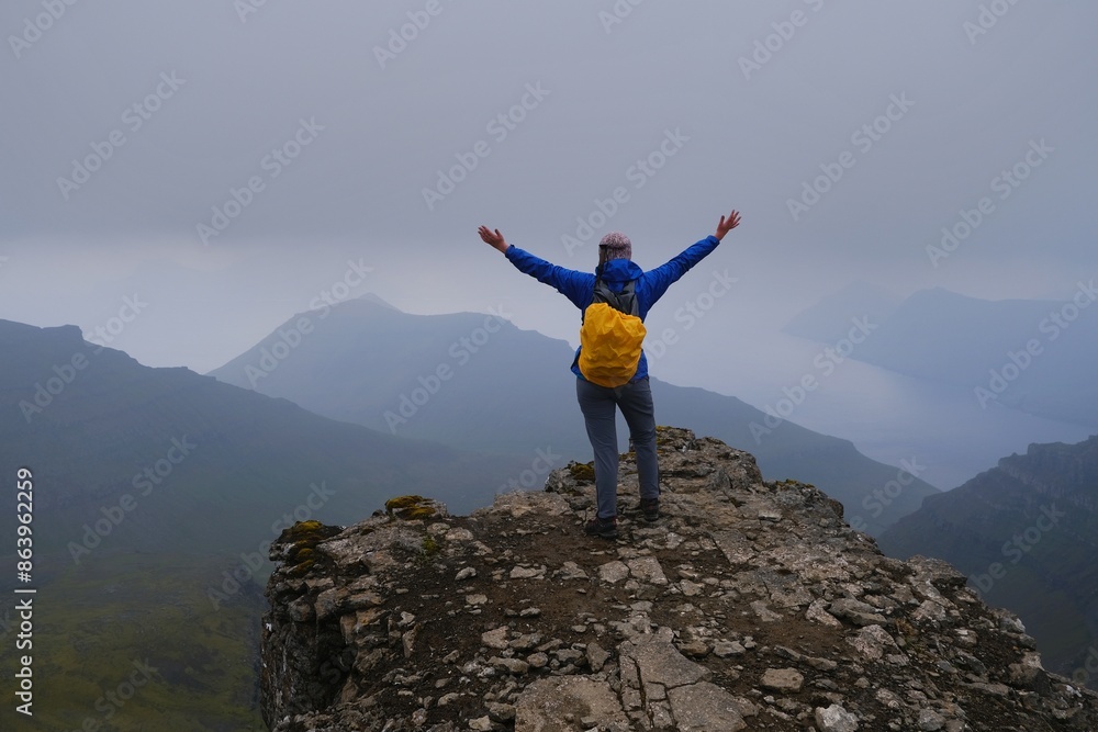 Obraz premium Silhouette of person on peak on foggy day. Eysturoy Island and climbing highest peak of Faroe Islands - Slættaratindur, Denmark. 