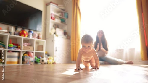 A mom teaches her baby to crawl. Child toddler walk concept. A baby crawls on the floor and takes the first steps. A mom teaches her baby how to crawl and how to do it in first few lifestyle steps. photo