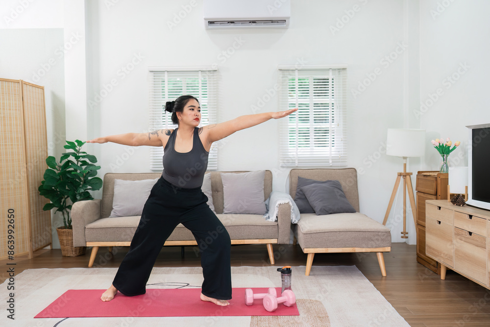Obraz premium Overweight Woman Practicing Yoga at Home for Wellness and Fitness in a Modern Living Room