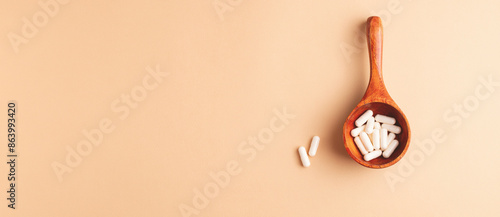 Top view of wooden spoon with white capsules on beige background. Minimalist healthcare and wellness concept, banner for web site.