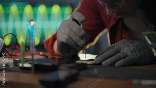 To correct. An electronic technician wearing protective gloves focuses on using a screwdriver in an electronics workshop. Electronics service technician unscrews screws performs service, work