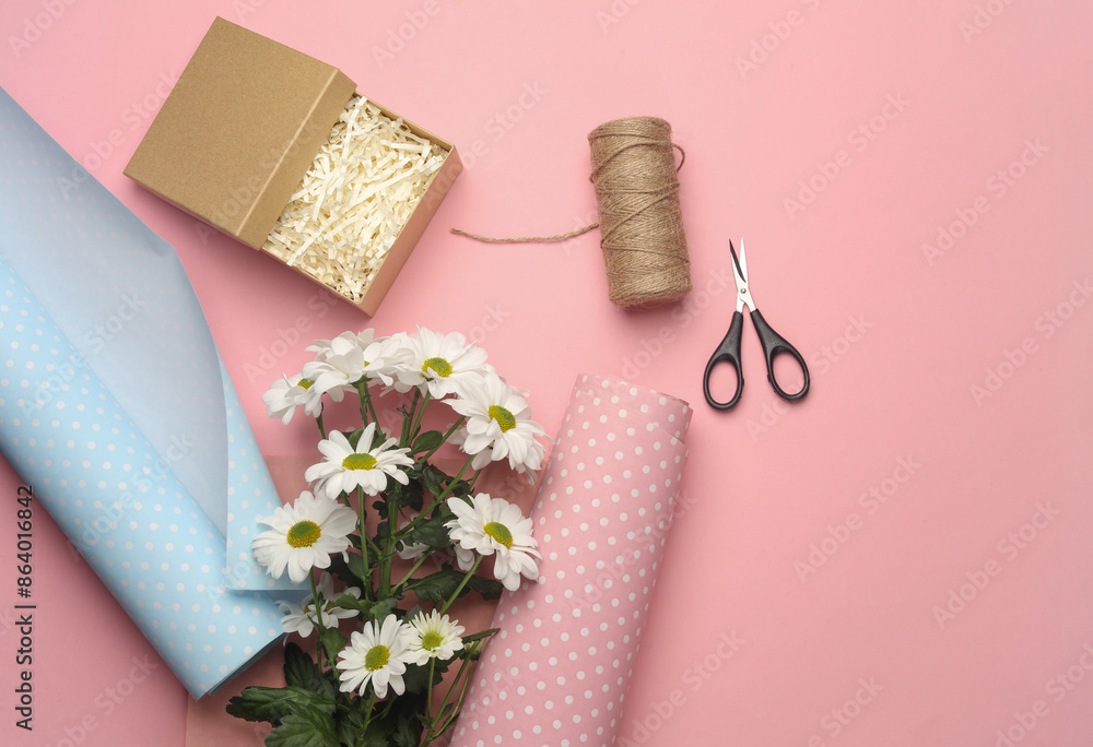 Wrapping paper with flowers and a box, a skein of thread and scissors on a pink background. Flat lay Wrapping paper with flowers and a box, a skein of thread and scissors on a pink background. Flat lay