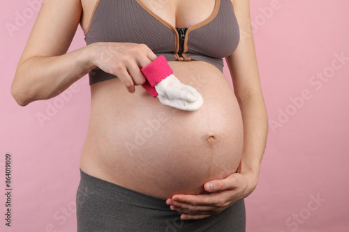 Pregnant woman holding a pair of socks on pink background photo
