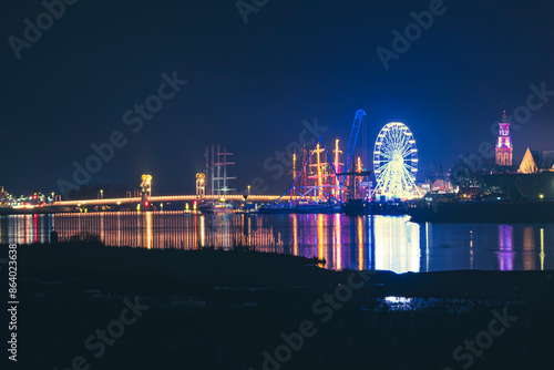 Nightscape of old city (Kampen) along river in the Netherlands with the lighting of a Ferris wheel and a sailing event