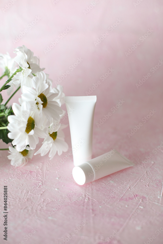 White tubes of cream with a bouquet of flowers on a pink background White tubes of cream with a bouquet of flowers on a pink background