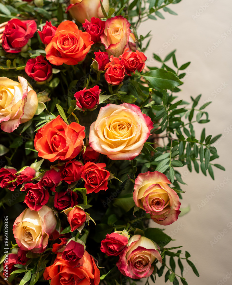 Obraz premium Part of a large bouquet of red, orange and yellow roses with green sprigs