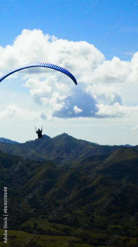 4k ultra hd. Two People ride gliding Paramotor paraglide paraplane fly in the sky with mountains midday sunny. Blue clouds. Vertical shot. 4k ultra hd. Two People ride gliding Paramotor paraglide paraplane fly in the sky with mountains midday sunny. Blue clouds. Vertical shot.
