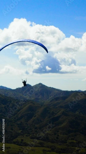 4k ultra hd. Two People ride gliding Paramotor paraglide paraplane fly in the sky with mountains midday sunny. Blue clouds. Vertical shot. photo