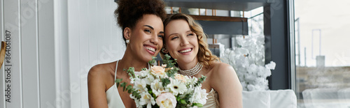 Two brides, one holding a bouquet, smile radiantly on their wedding day.