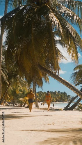4k ultrahd. Young pretty stunning ideal Sexy woman and man walking near palm trees on white beach in Saona island dominican republic. Sunny midday wideshot. No faces. Relaxing Vertical shot.