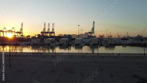 The Rock of Gibraltar rises majestically across the bustling cargo port of Algeciras, its shadow stretching over towering cranes and colorful containers.