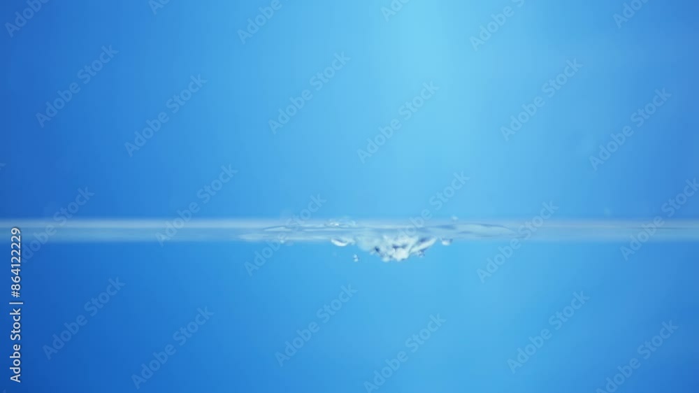 Splattering water creating tiny droplets and ripples in a container filled with water against a blue background. Splattering water creating tiny droplets and ripples in a container filled with water against a blue background.