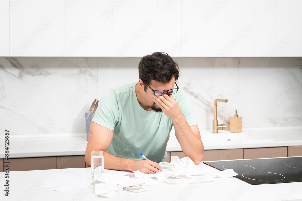 Obraz premium Close up of unhappy man sitting at the table, stressed and confused by calculate expense from invoice or bills, have no money to pay mortgage or loan. High prices and spending money concept