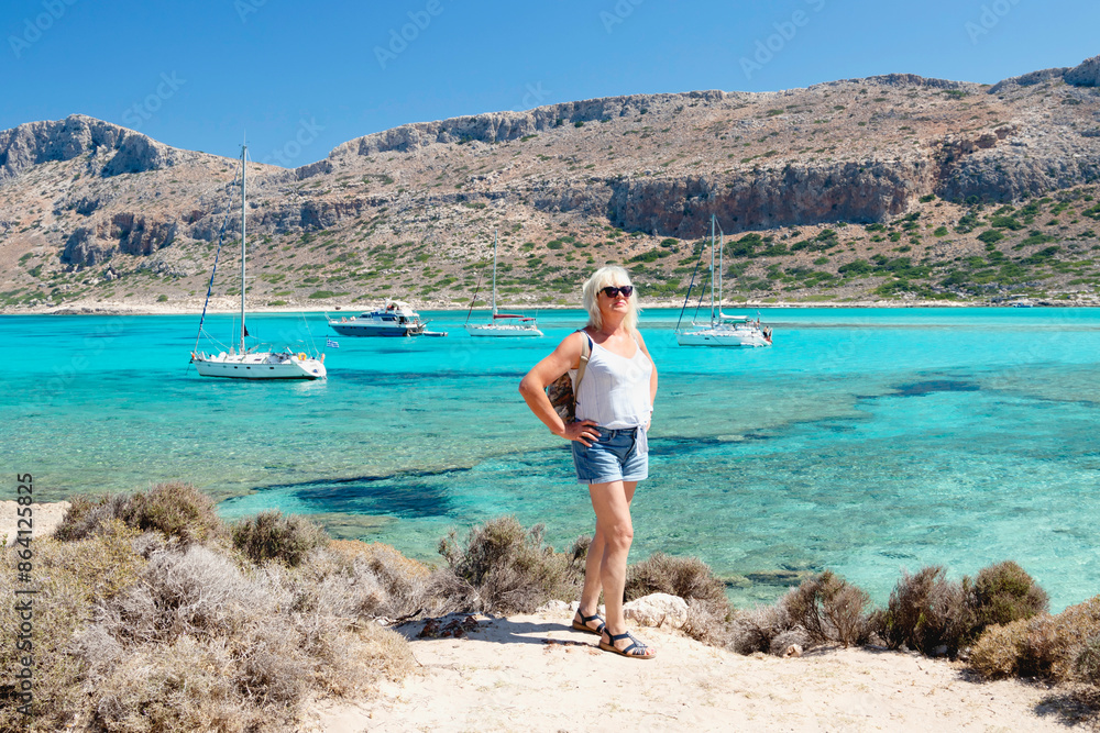 Happy senior female hiker enjoying outdoor activity on the sea and mountain landscape. Greece. Balos. Crete. Happy senior female hiker enjoying outdoor activity on the sea and mountain landscape. Greece. Balos. Crete.