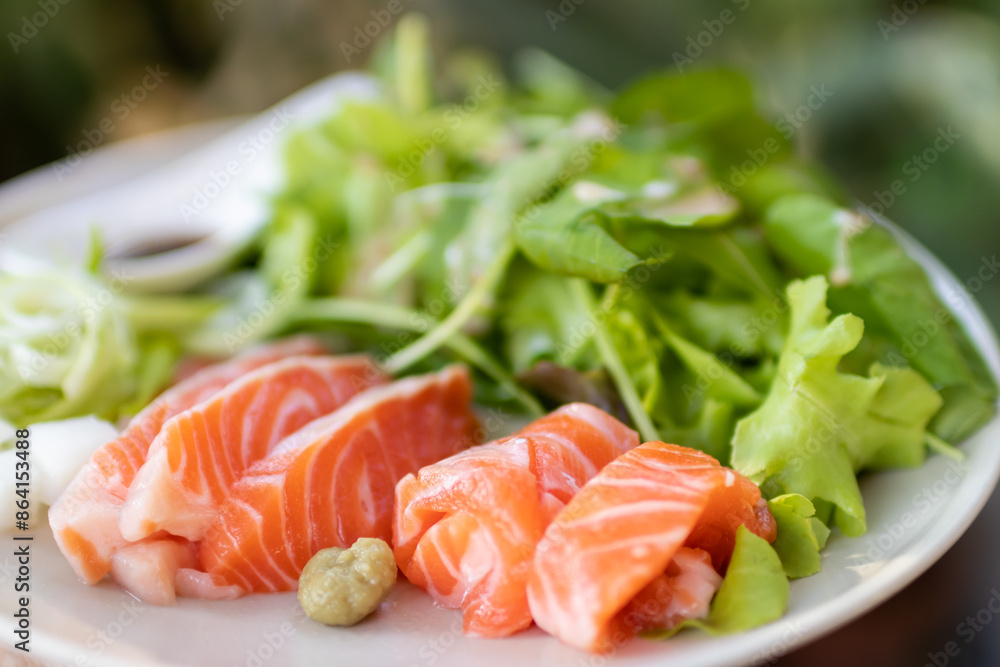 A plate of delicious-looking salmon sashimi. The salmon is served on a bed of lettuce and garnished with wasabi and pickled ginger. A plate of delicious-looking salmon sashimi. The salmon is served on a bed of lettuce and garnished with wasabi and pickled ginger.