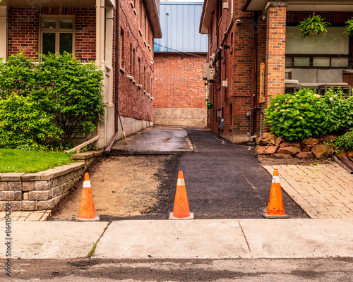 ashpalt driveway repaving project in progress on shared laneway between to residences on established city street shot in toronto beaches neighbourhood in summer photo