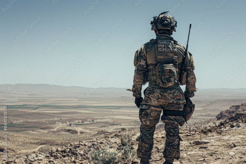 A soldier is seen standing firmly in a desert landscape, the clear sky above adding to the raw and unfiltered feel of the photograph. A soldier is seen standing firmly in a desert landscape, the clear sky above adding to the raw and unfiltered feel of the photograph.