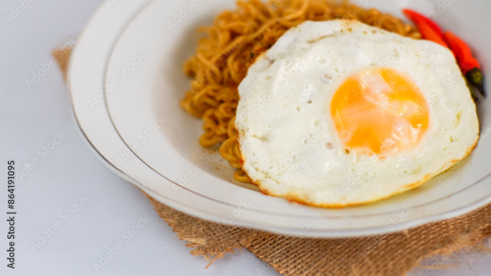 Fried noodles with fried egg and red cayenne pepper. Served on a serving white plate. Isolated on white background. Fried noodles with fried egg and red cayenne pepper. Served on a serving white plate. Isolated on white background.