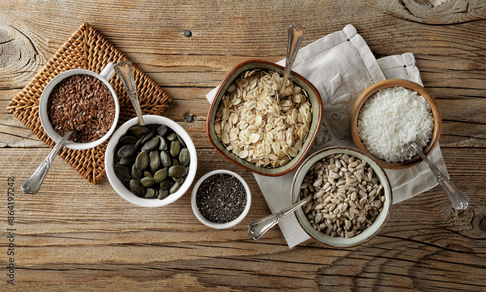 Variety of seeds and ingredients for a healthy diet. Bowls with flax seeds, pumpkin, chia, oats, sunflower and dehydrated coconut flakes on old wooden background. Top view, space for text, flat lay. Variety of seeds and ingredients for a healthy diet. Bowls with flax seeds, pumpkin, chia, oats, sunflower and dehydrated coconut flakes on old wooden background. Top view, space for text, flat lay.