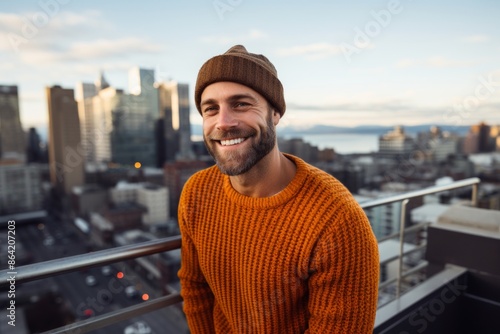 Portrait of a cheerful man in his 30s dressed in a warm wool sweater while standing against vibrant city skyline