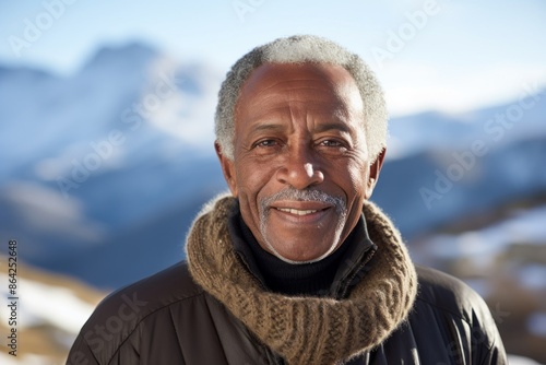 Portrait of a glad afro-american elderly man in his 90s wearing a classic turtleneck sweater isolated in snowy mountain range