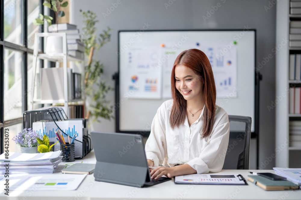 A woman is sitting at a desk with a laptop and a white board behind her A woman is sitting at a desk with a laptop and a white board behind her