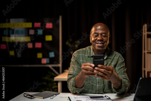 A man is sitting at a desk with a cell phone in his hand