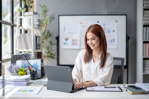 A woman is sitting at a desk with a laptop and a white board behind her © Wasana