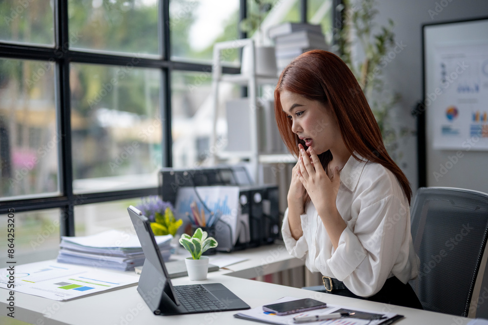Obraz premium A woman is sitting at a desk with a laptop and a cell phone