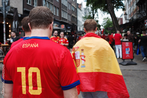 Selective Spanish flag and spanish football shirt are wear by football fan who walk in old town. 