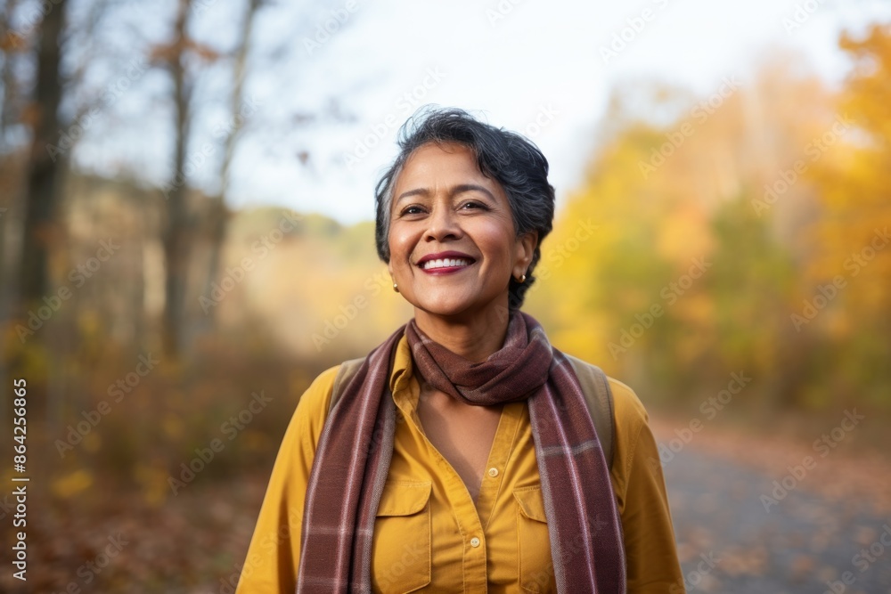 Portrait of a cheerful indian woman in her 50s sporting a vintage band t-shirt in background of autumn leaves Portrait of a cheerful indian woman in her 50s sporting a vintage band t-shirt in background of autumn leaves