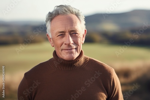 Portrait of a satisfied man in his 80s wearing a classic turtleneck sweater in front of quiet countryside landscape