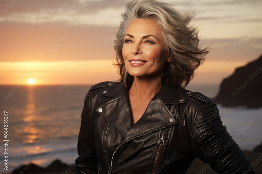 Portrait of a jovial woman in her 60s sporting a classic leather jacket while standing against beautiful beach sunset Portrait of a jovial woman in her 60s sporting a classic leather jacket while standing against beautiful beach sunset