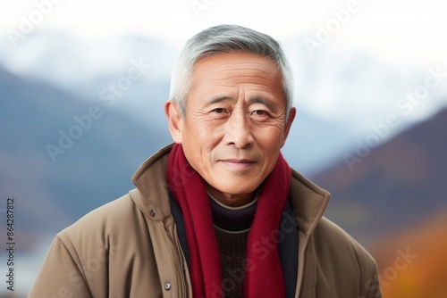 Portrait of a tender asian man in his 60s dressed in a warm wool sweater while standing against backdrop of mountain peaks