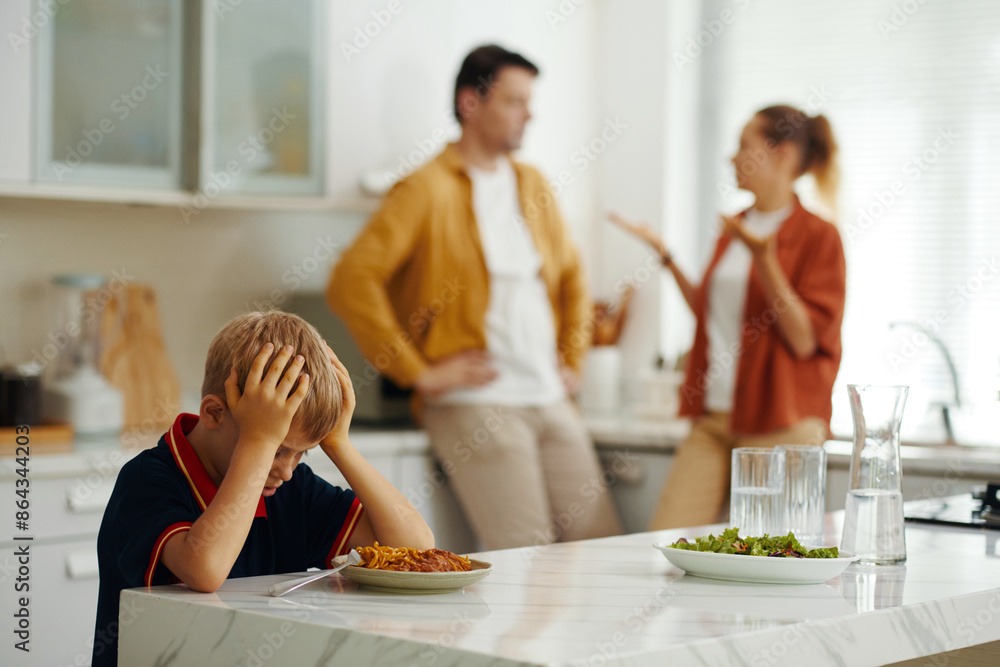 Upset child tired of conflict of his parents while they arguing in background during lunch Upset child tired of conflict of his parents while they arguing in background during lunch