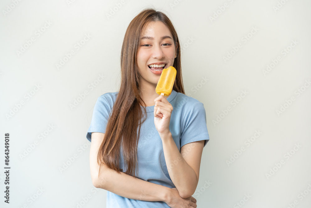 Cheerful enjoy, happy cute asian woman wearing casual with brunette hair, eating popsicle, teenage girl holding ice pop, lolly frozen stick with mango yellow, passion fruit ice cream tasty in summer. Cheerful enjoy, happy cute asian woman wearing casual with brunette hair, eating popsicle, teenage girl holding ice pop, lolly frozen stick with mango yellow, passion fruit ice cream tasty in summer.