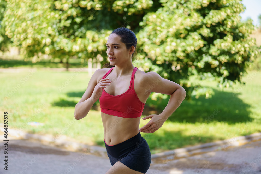 A dedicated young woman is jogging in the park, committed to her fitness and health routine during summer A dedicated young woman is jogging in the park, committed to her fitness and health routine during summer