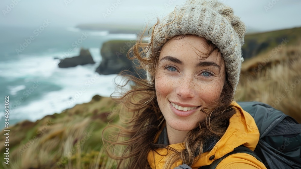 A smiling woman in a yellow jacket and beanie takes a selfie with rugged coastal cliffs and a choppy ocean, enjoying the serene and wild natural landscape. A smiling woman in a yellow jacket and beanie takes a selfie with rugged coastal cliffs and a choppy ocean, enjoying the serene and wild natural landscape.