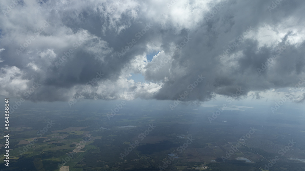 A bird's-eye perspective of a sky filled with clouds, a plane in the foreground, and a field below A bird's-eye perspective of a sky filled with clouds, a plane in the foreground, and a field below