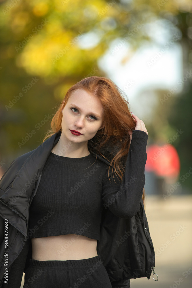 Portrait of a young beautiful red-haired girl in dark clothes outdoors. Portrait of a young beautiful red-haired girl in dark clothes outdoors.