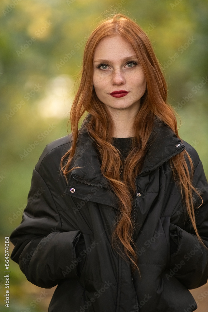 Portrait of a young beautiful red-haired girl in dark clothes outdoors. Portrait of a young beautiful red-haired girl in dark clothes outdoors.