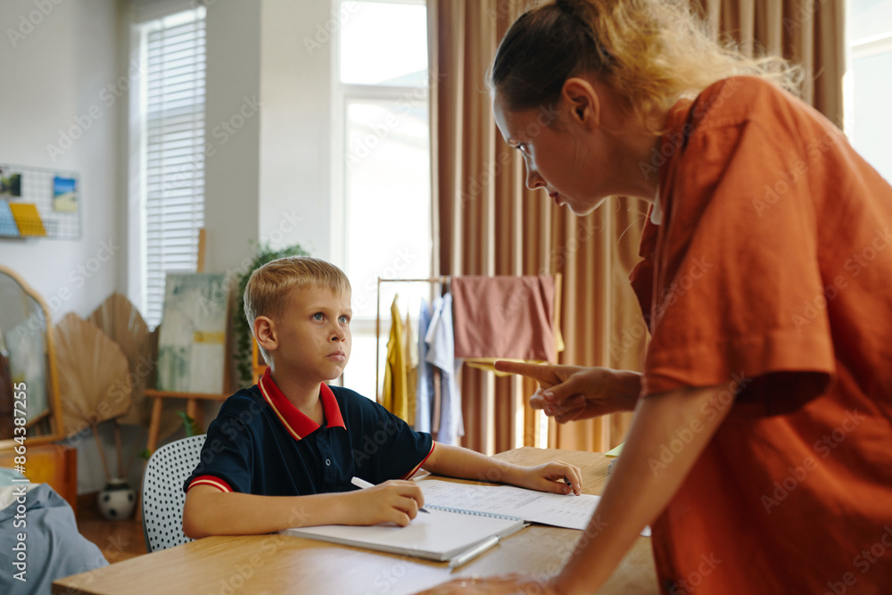 Mom explaining the importance of study to her son while he sitting at desk Mom explaining the importance of study to her son while he sitting at desk