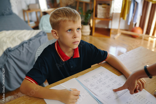 Mom forcing her child to do homework while he sitting at desk in the room