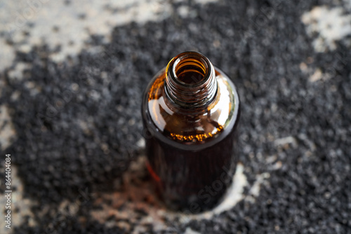 Black cumin or Nigella sativa seed oil in a dark glass bottle on a table photo