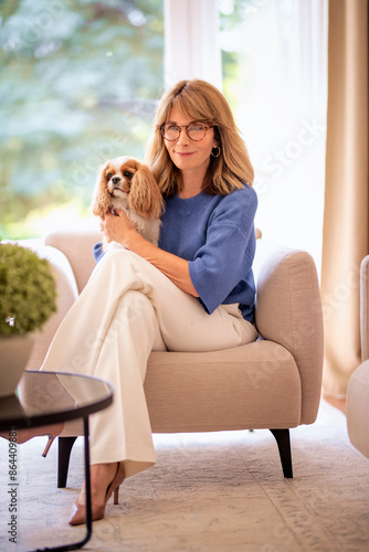 Mid aged woman with her puppy relaxing in an armchair in her modern home photo