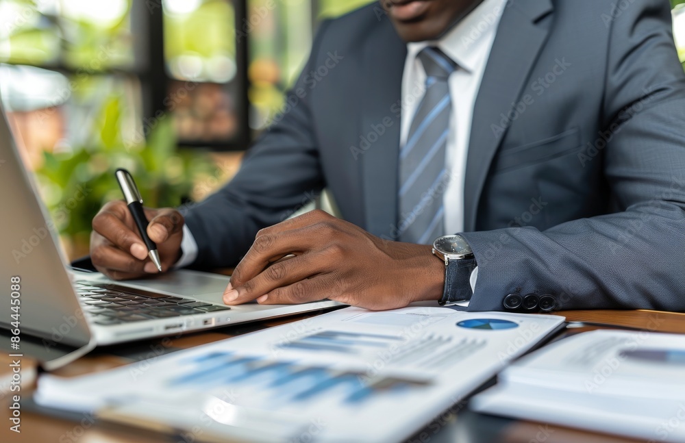 Businessman Working on Laptop With Financial Documents in Office Businessman Working on Laptop With Financial Documents in Office