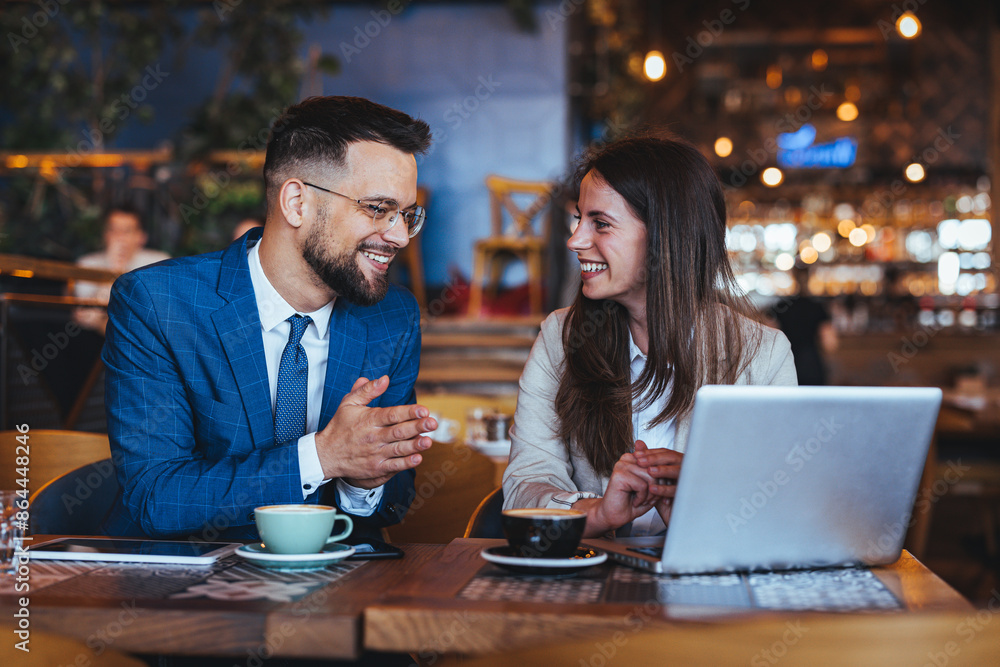 A man and woman dressed in business attire engage in discussion over a laptop in a bustling coffee house, reflecting a modern work environment where professionals often convene. A man and woman dressed in business attire engage in discussion over a laptop in a bustling coffee house, reflecting a modern work environment where professionals often convene.