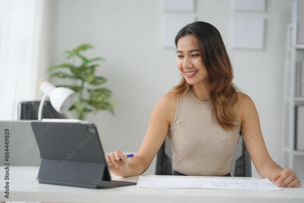 Smiling woman working on a tablet at her desk, engaged in remote work, surrounded by a modern office setup and greenery. Smiling woman working on a tablet at her desk, engaged in remote work, surrounded by a modern office setup and greenery.