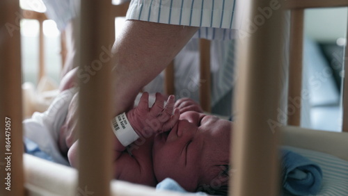 Mother’s hands gently caring for a newborn baby lying in a bassinet, visible through crib bars, capturing the intimate and delicate moments of infant care, emphasizing the nurturing bond