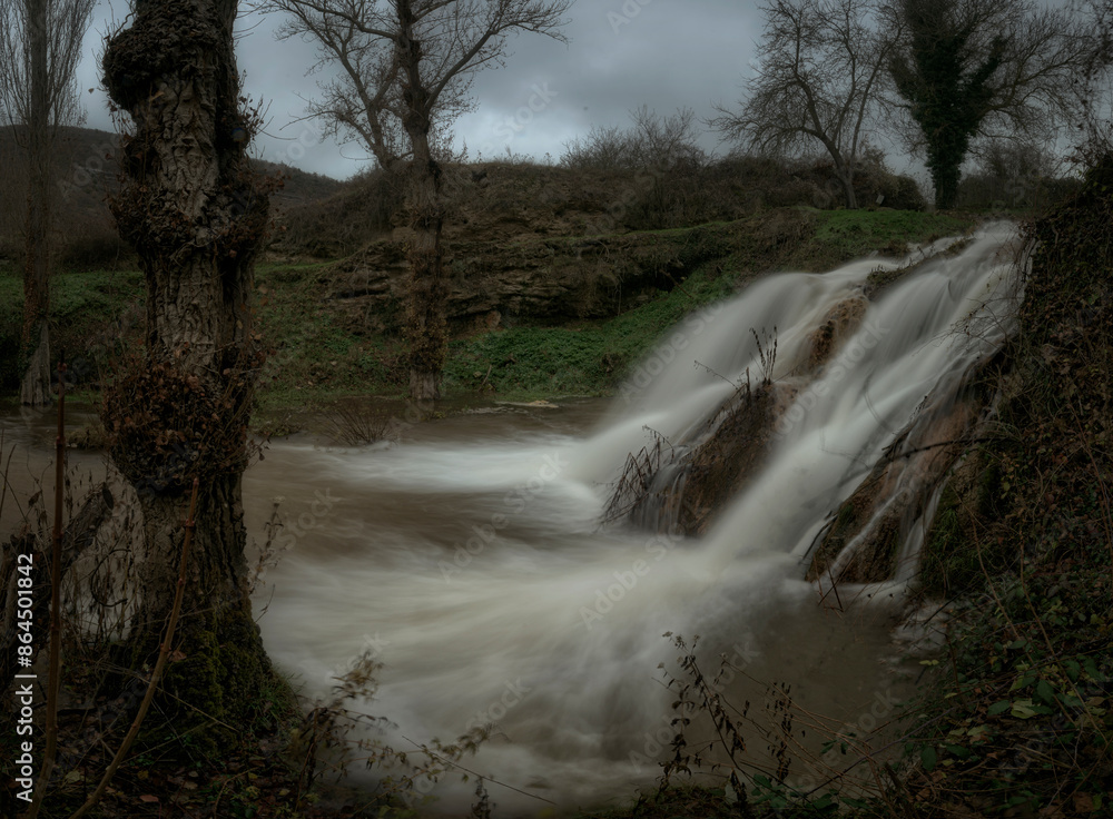 Side view of the Tubilla del Agua waterfall, Burgos, between the trees, falling forcefully on the Rudron river Side view of the Tubilla del Agua waterfall, Burgos, between the trees, falling forcefully on the Rudron river